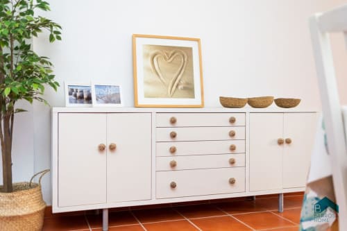 Mobiliario blanco moderno con tiradores de madera en apartamento Barrosa Home, con arte decorativo de corazón y planta en maceta