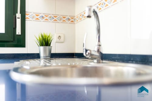 Fregadero moderno con grifo, armarios verdes y azulejos decorativos en el apartamento Barrosa Home de España