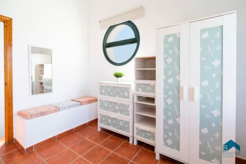 Dormitorio moderno en Barrosa Home con camas gemelas, unidades de almacenamiento con paneles florales y ventana circular