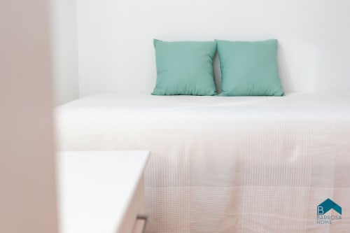 Cojines turquesas en cama blanca en apartamento Barrosa Home, España