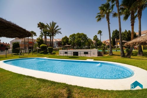 Piscina ovalada del resort Barrosa con palmeras, zona de descanso y cabañas blancas en España