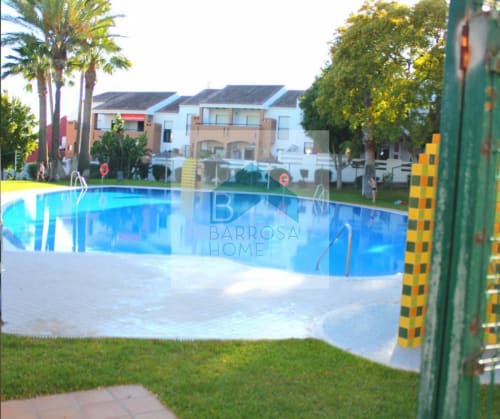 Piscina Barrosa Home con agua azul, tumbonas blancas, palmeras y modernos edificios de apartamentos con portones verdes