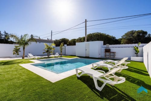 Zona de piscina de Villa Granizo en Barrosa Home con tumbonas, jardín verde y arquitectura blanca en España