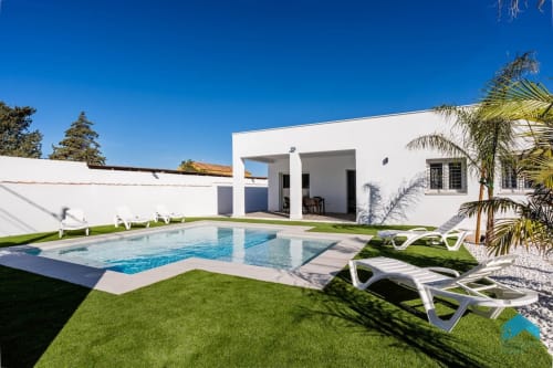 Villa blanca moderna con piscina, tumbonas, palmeras y jardín bien cuidado en Barrosa Home
