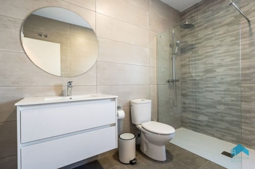 Baño moderno en Villa Granizo C de Barrosa Home con espejo redondo, vanidor blanco, inodoro y ducha abierta