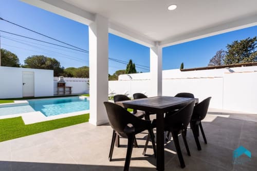 Patio cubierto Villa Granizo C con mesa de comedor negra, cuatro sillas, piscina y jardín en Barrosa Home, España