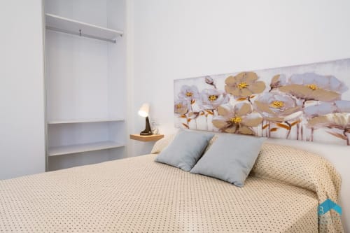 Dormitorio moderno en Villa Granizo C de Barrosa Home con obras de arte floral, almohadas azules y estantería minimalista blanca