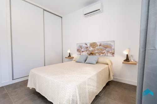 Dormitorio moderno en Villa Granizo C de Barrosa Home con ropa de cama crema, almohadas azules, arte floral y armario empotrado, España