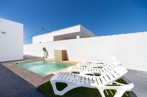 Villa Bison Una terraza con tumbonas, piscina climatizada y arquitectura moderna blanca en Barrosa Home, España