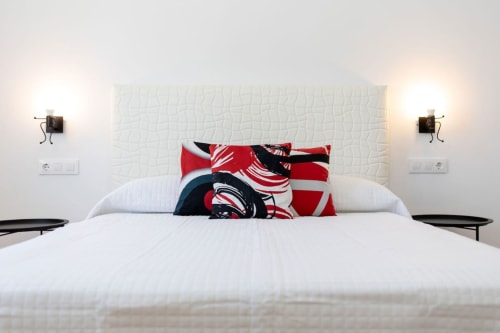 Dormitorio moderno en Barrosa Home Villa Bison A con cama blanca, cabecero texturizado, almohadas con patrón rojo y apliques de pared