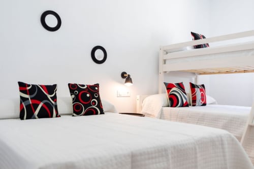Dormitorio moderno en villa Barrosa Home con camas blancas, cojines decorativos rojo y negro, y decoración minimalista en paredes