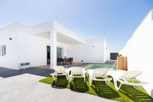 Villa Bison A en Barrosa Home: elegante villa blanca con patio, tumbonas, piscina, zona de comedor y jardín perfectamente cuidado