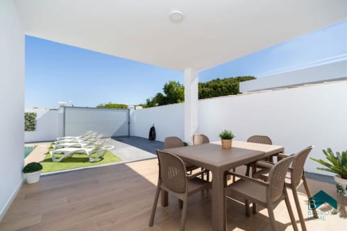 Terraza moderna de la villa Barrosa Home con mesa de comedor, tumbonas y vista a la piscina