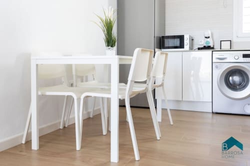 Moderna zona de cocina-comedor en la villa Barrosa Home con mesa blanca, sillas, electrodomésticos y planta en maceta