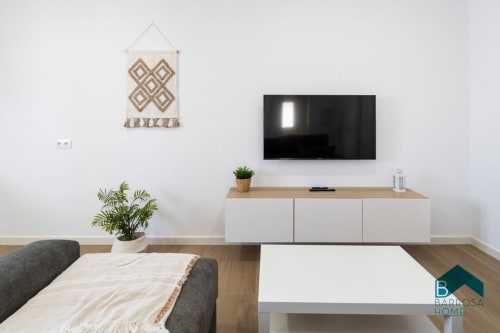 Moderno salón del apartamento Barrosa Home con televisor de pared, consola blanca, plantas decorativas y diseño minimalista