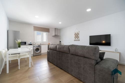 Apartamento moderno de planta abierta en Barrosa Home con sofá gris, mesa de comedor, cocina, lavadora, TV mural y madera