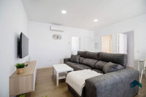 Sala moderna de la villa Barrosa Home con sofá gris seccionado, televisor montado en pared y decoración minimalista