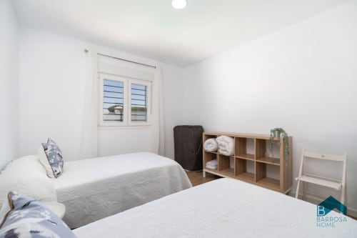 Dormitorio luminoso en villa Barrosa Home con dos camas, estanterías de madera, paredes blancas y ventana con contraventanas azules