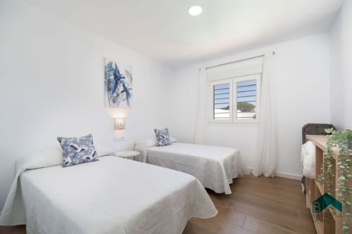 Luminoso dormitorio doble en villa Barrosa Home con camas blancas, acentos azules, piso de madera y vistas al mar