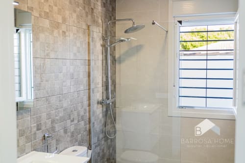 Baño moderno con ducha a ras de suelo, mamparas de cristal y ventana en la villa Barrosa Home de España