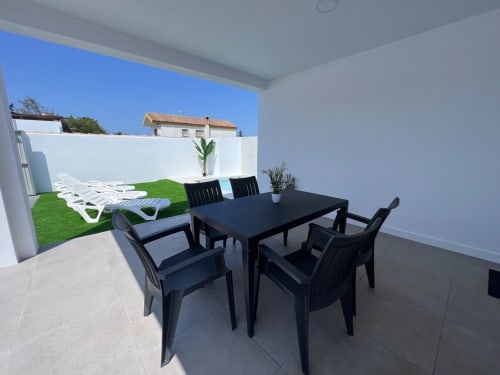 Terraza de la Villa Granizo en Barrosa Home con mesa de comedor negra, sillas y tumbonas blancas con vistas al jardín