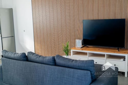 Sala moderna de la villa Barrosa Home con sofá azul, TV, pared de acento de madera y zona de cocina integrada