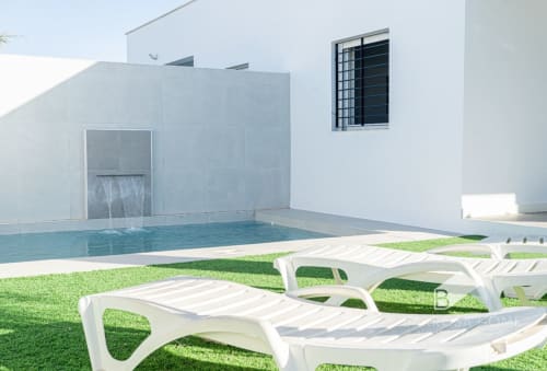 Villa moderna con piscina, tumbonas blancas en el jardín y arquitectura minimalista en Barrosa Home