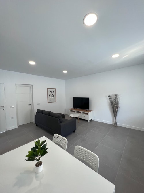 Sala de estar moderna de planta abierta en Villa Granizo de Barrosa Home con sofá negro, mesa de comedor y televisor en España
