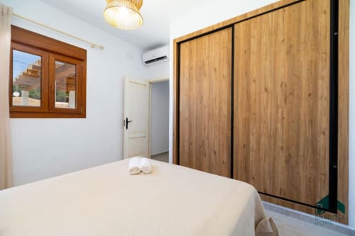 Dormitorio moderno en villa Barrosa Home con armario de madera, cama y marco de ventana de madera