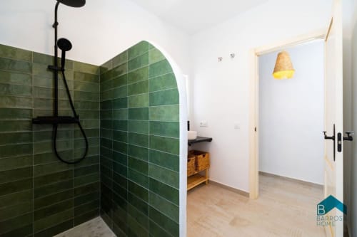 Baño moderno con zona de ducha de azulejos verdes, accesorios negros y almacenamiento de madera en villa Barrosa Home en España