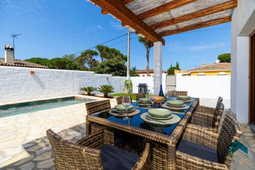 Terraza de la villa Barrosa con mesa de comedor, piscina y pérgola de madera bajo cielo azul