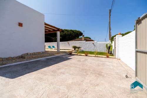 Villa Barrosa con paredes blancas, patio, tumbonas y exuberante paisajismo bajo cielo azul despejado