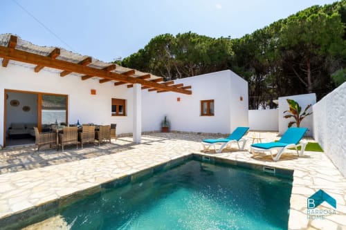 Villa Barrosa con piscina turquesa, paredes blancas, pérgola de madera, tumbonas y jardín mediterráneo
