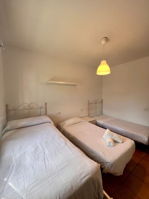 Dormitorio luminoso en villa Barrosa Home con tres camas, lámpara colgante amarilla y piso de barro cocido