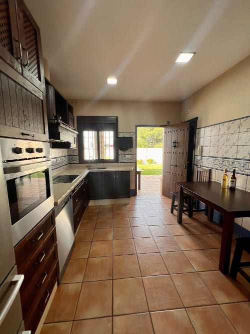 Amplia cocina en Villa Pinar del Edén con muebles de madera oscura, electrodomésticos de acero inoxidable y piso de azulejos de terracota