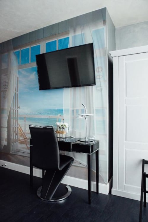 Modern hotel room at Hôtel Amirauté La Baule with wall-mounted TV, desk, black chair, and ocean view wallpaper