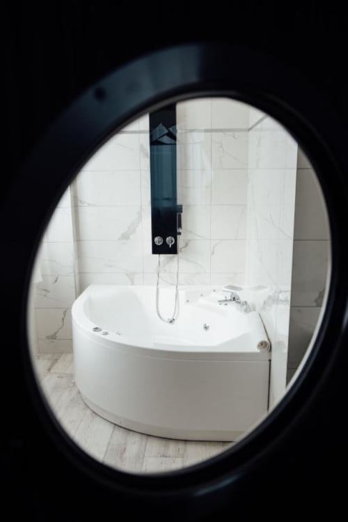 Modern spa bathtub with black rainfall shower at Hôtel Amirauté la Baule, viewed through circular bathroom window