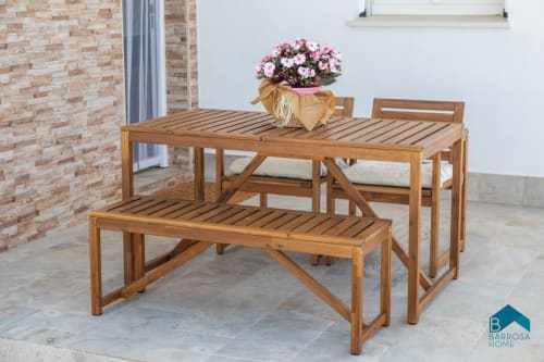 Comedor de madera en el patio de Barrosa Home con mesa, banco, sillas y flores rosas