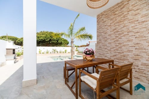 Patio moderno en Barrosa Home con mesa de comedor en madera, pared de ladrillo y vistas a la piscina en España