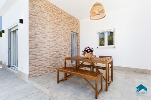 Patio exterior de Barrosa Home con mesa de comedor de madera, asientos de banco, pared de ladrillo y lámpara colgante tejida