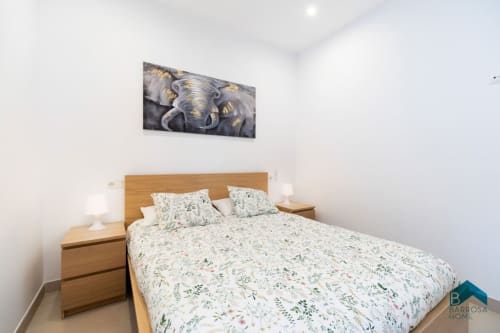 Dormitorio en Barrosa Home con cama de madera, ropa de cama floral, mesillas de noche y obra de arte de elefantes sobre el cabecero