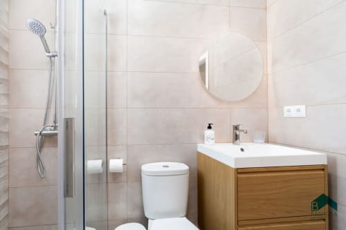 Baño moderno en apartamento Barrosa Home con ducha tipo walk-in, lavamanos blanco, inodoro y espejo redondo