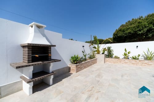 Moderna zona de barbacoa exterior en el apartamento Barrosa Home con paredes blancas, chimenea de ladrillo y jardín mediterráneo