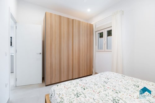 Dormitorio moderno de Barrosa Home con ropa de cama floral, armario de puertas correderas de madera y paredes blancas