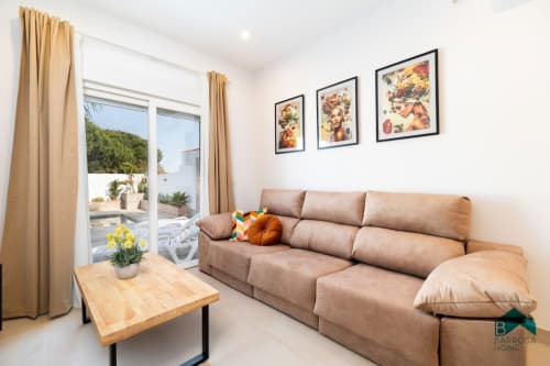 Salón moderno en Barrosa Home con sofá beige, mesa de madera y acceso a terraza con vista al jardín