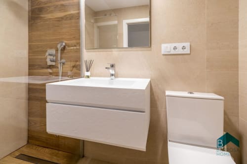 Baño moderno del apartamento Barrosa Home con tocador blanco, detalles de madera, espejo e inodoro