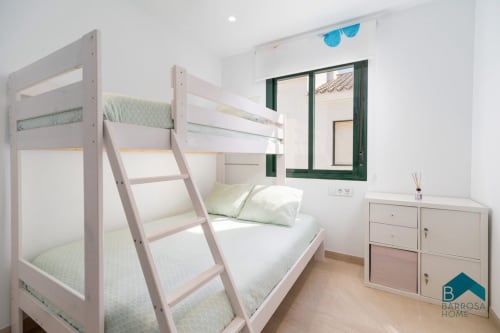 Dormitorio luminoso en Barrosa Home con literas blancas, almohadas verdes, escritorio de madera y ventana con marco verde