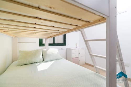 Dormitorio de estilo loft en apartamento Barrosa Home con cama elevada de madera, ropa de cama verde y muebles de almacenamiento blancos