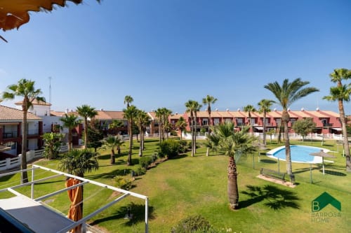 Complejo residencial Barrosa con palmeras, jardines verdes, piscina y edificios color terracota en España