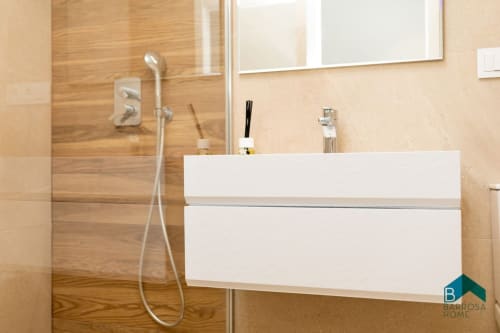 Baño moderno con vanidad blanca, paredes de azulejos de madera, ducha de cristal y espejo en el apartamento Barrosa Home en España